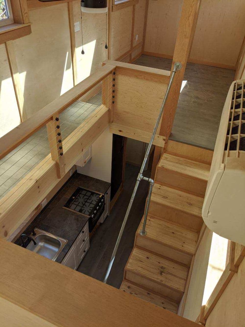 Interior view of a minimalist tiny house showcasing stairs, kitchen, and wooden finishes.