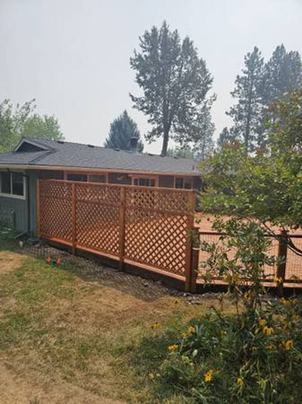 Wooden fence surrounding a backyard with a house and trees under smoky sky.