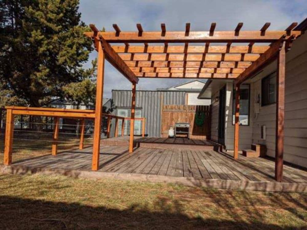 Wooden patio pergola with a spacious deck and grass area under a cloudy sky.