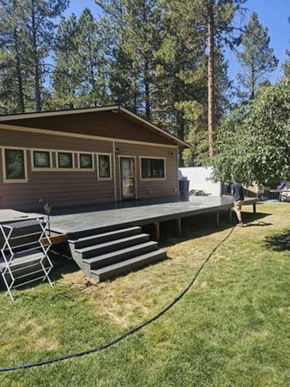 Home exterior featuring a spacious deck, steps, and a grassy yard surrounded by trees.