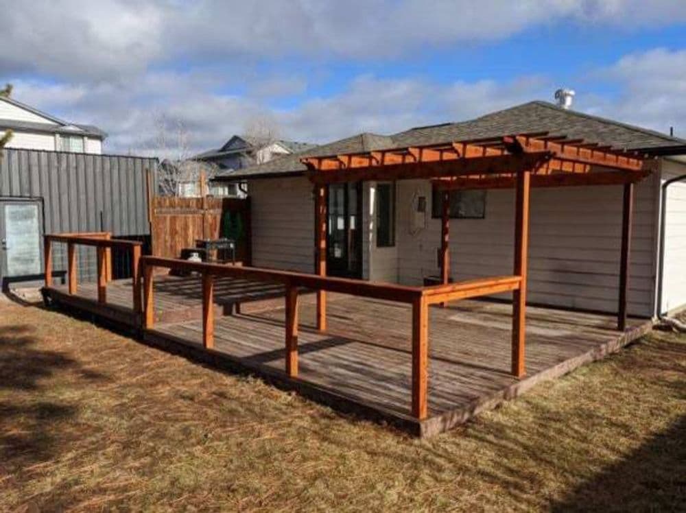 Wooden deck with railing and pergola attached to a house on a sunny day.
