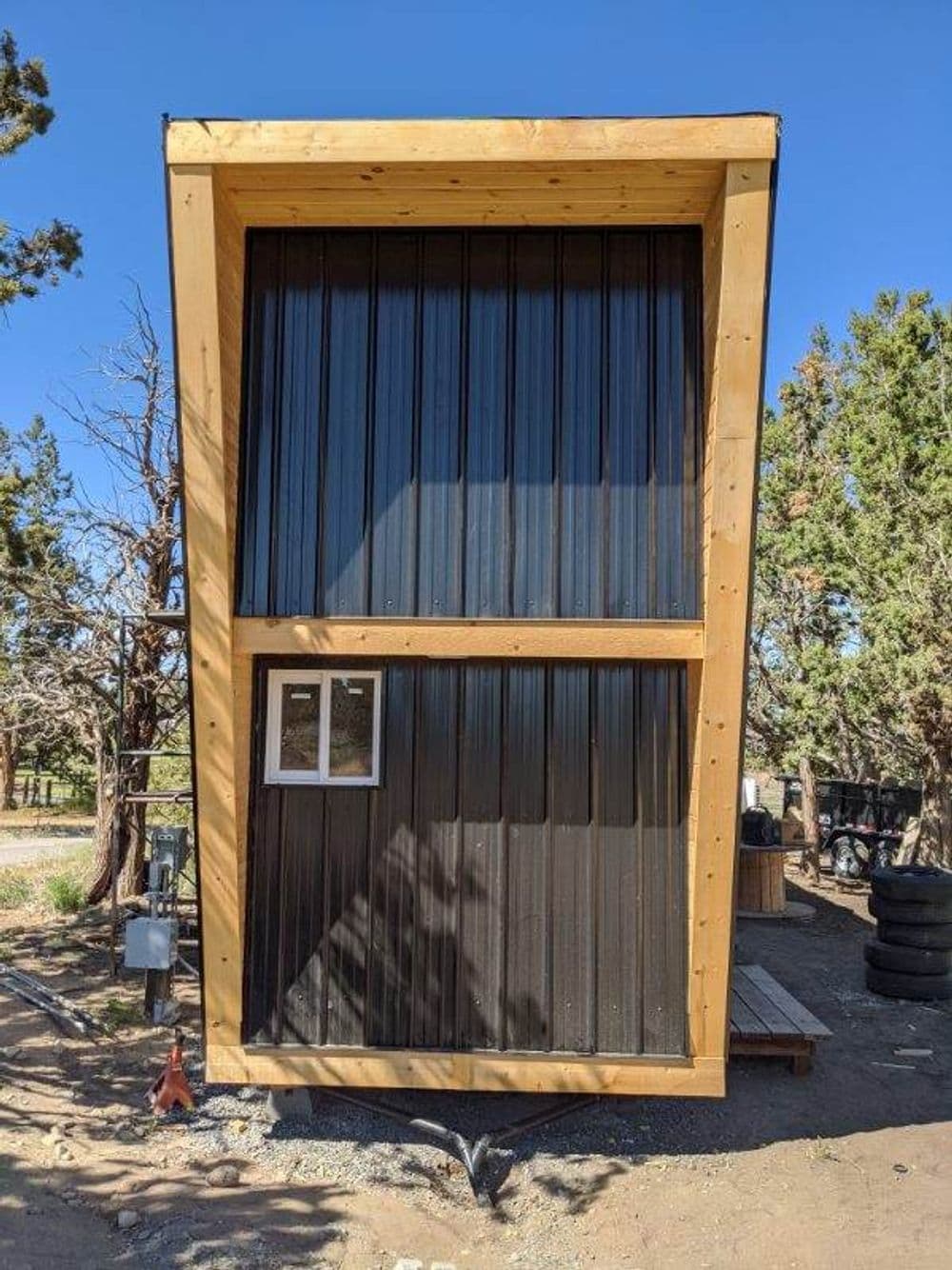 Modern tiny house with large windows and wooden frame, set in a natural landscape.