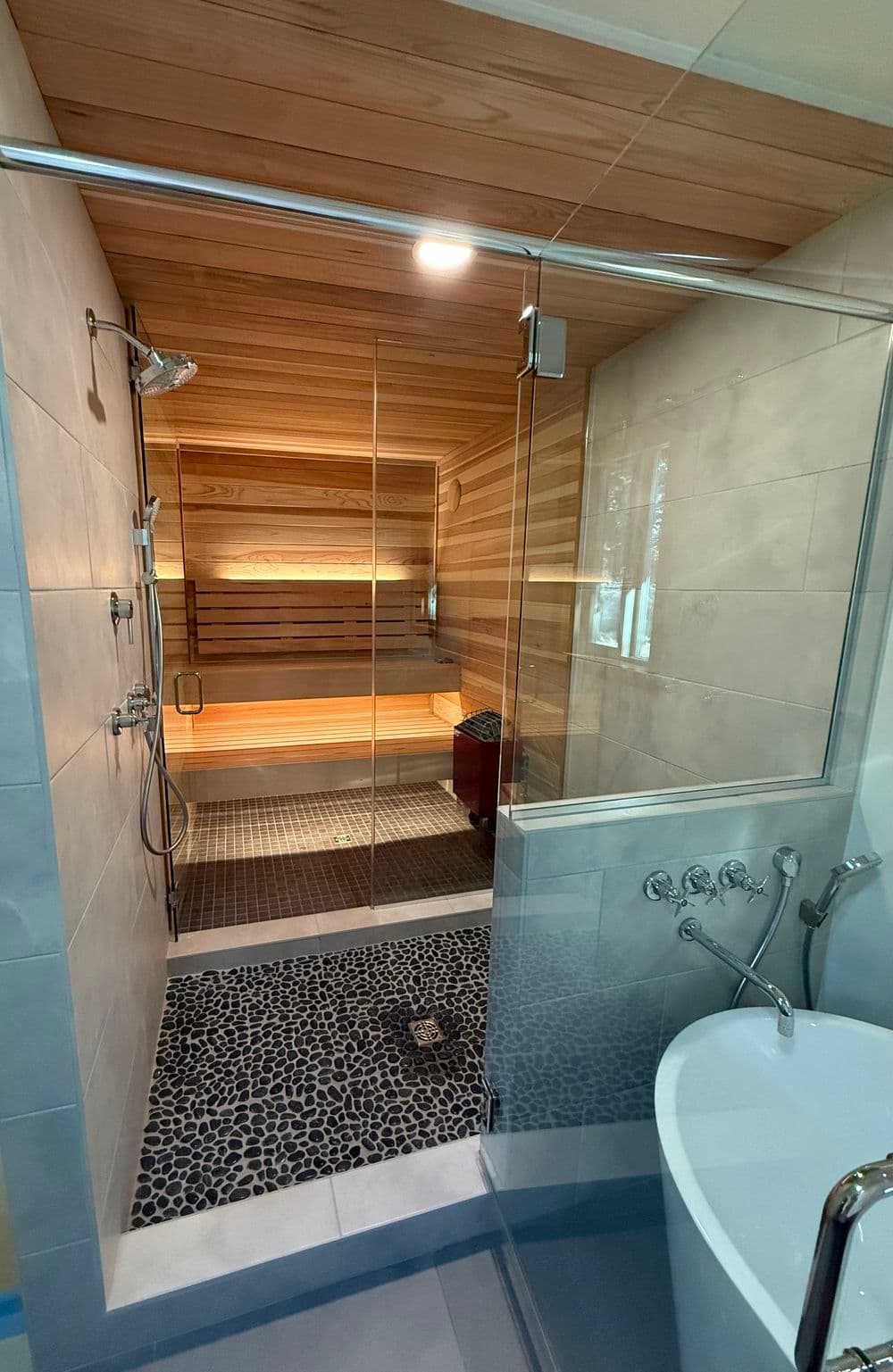 Modern bathroom featuring a glass shower, sauna area, and pebble stone floor.