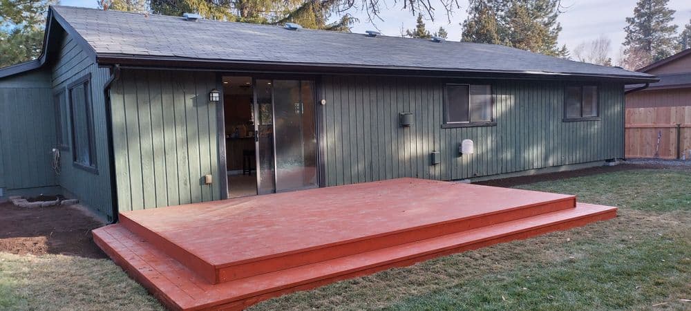 Modern green house exterior with a wooden deck and door leading into the home.