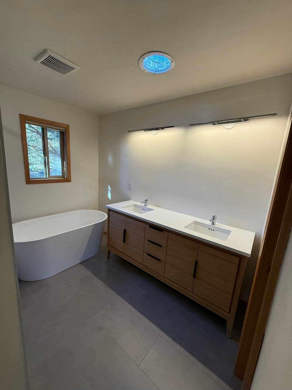 Modern bathroom with freestanding tub, double sink vanity, and natural light from window.