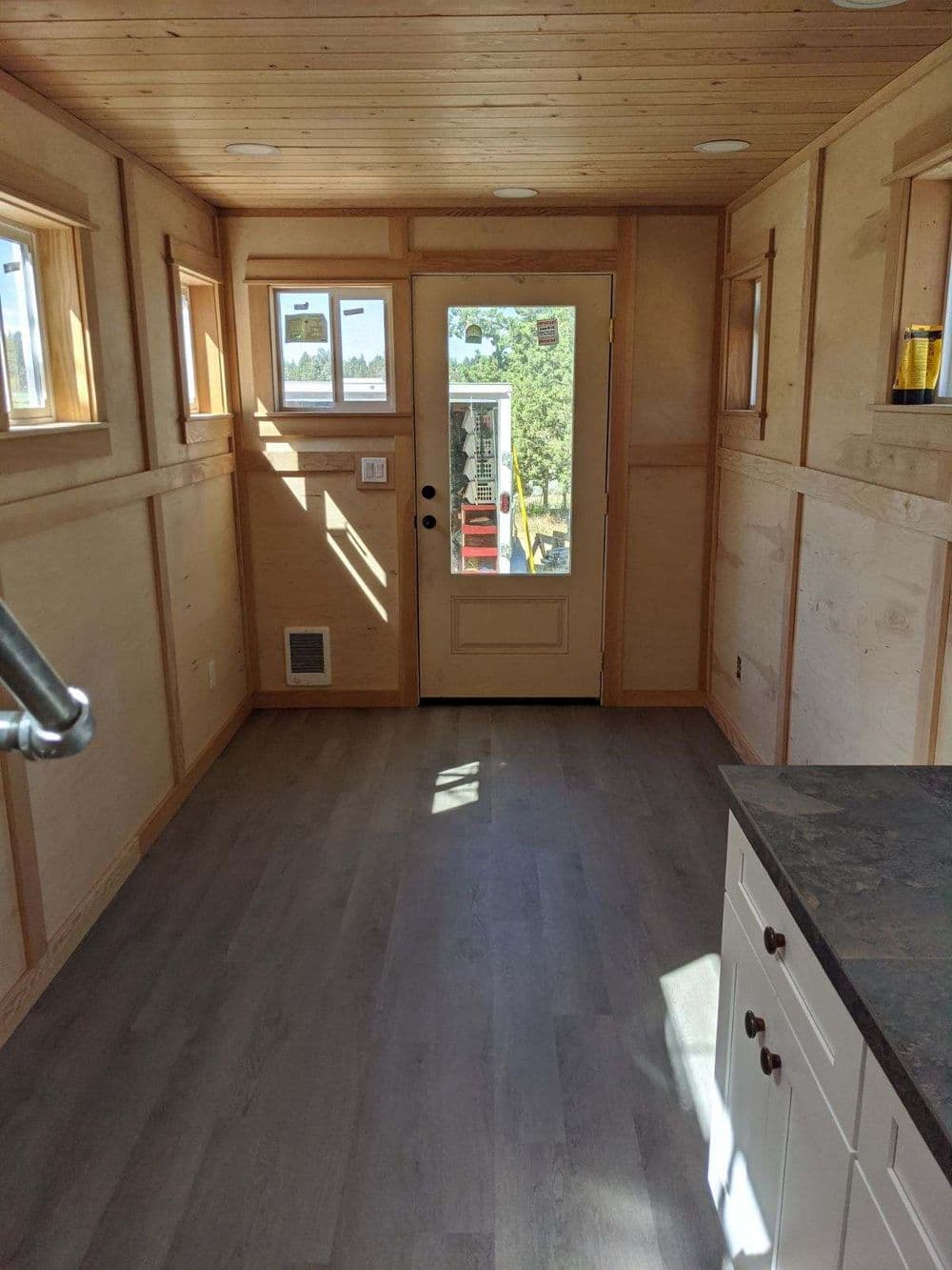 Bright tiny home interior with wood paneling and natural light from windows and door.