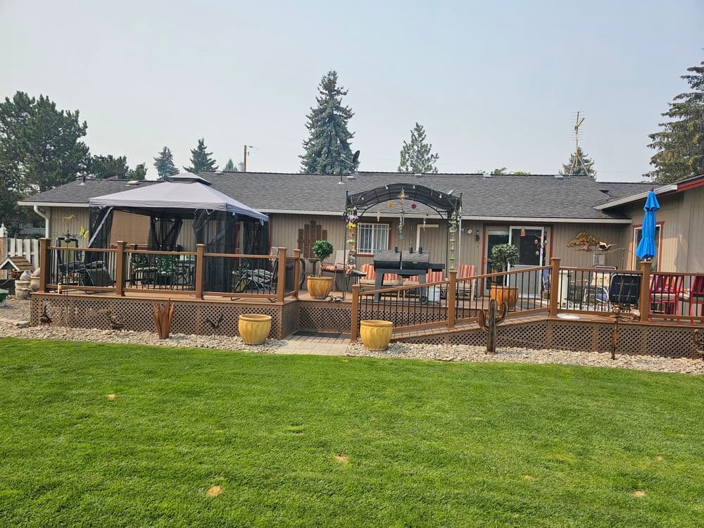 Modern backyard patio with dining area, gazebo, and lush green lawn in bright sunlight.