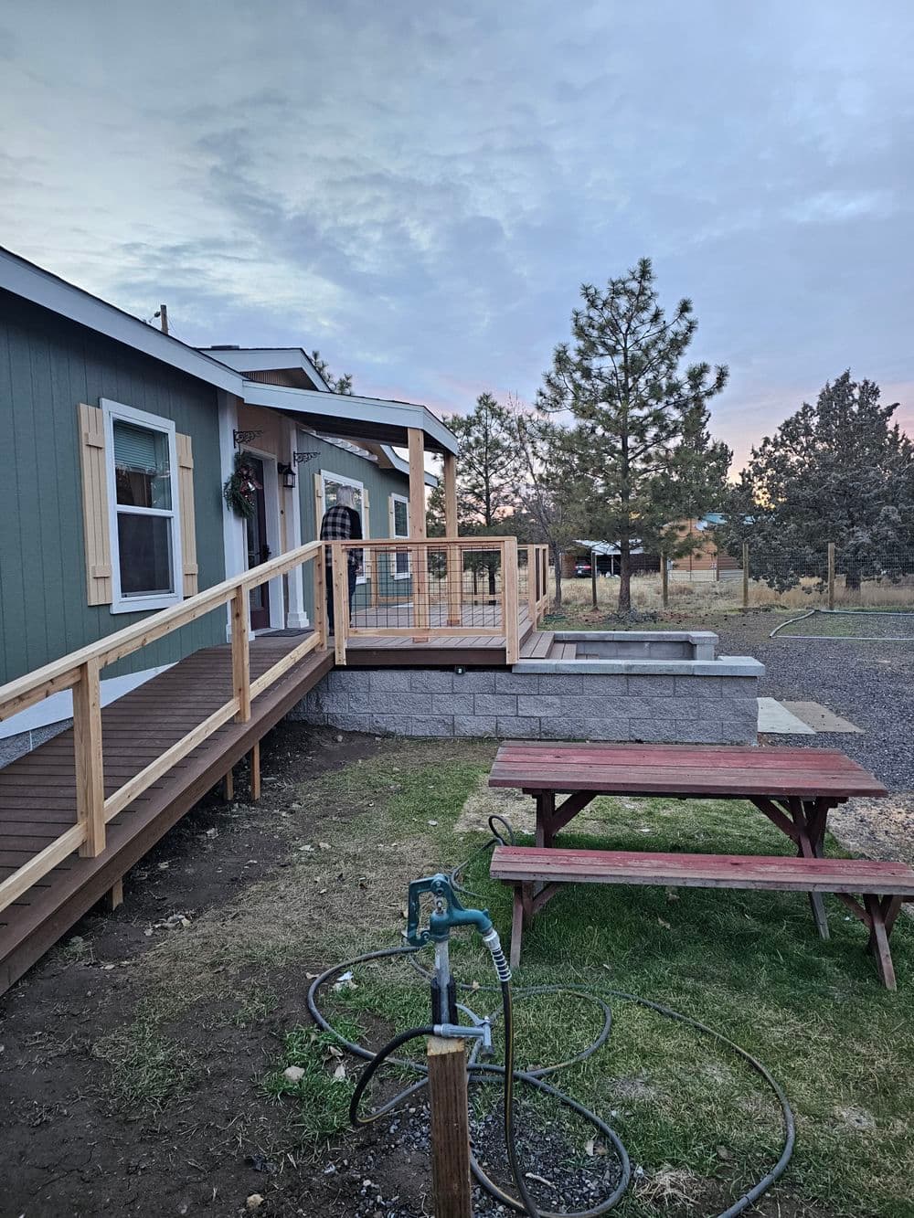 Modern home exterior with wooden deck, picnic table, and landscaped yard at sunset.
