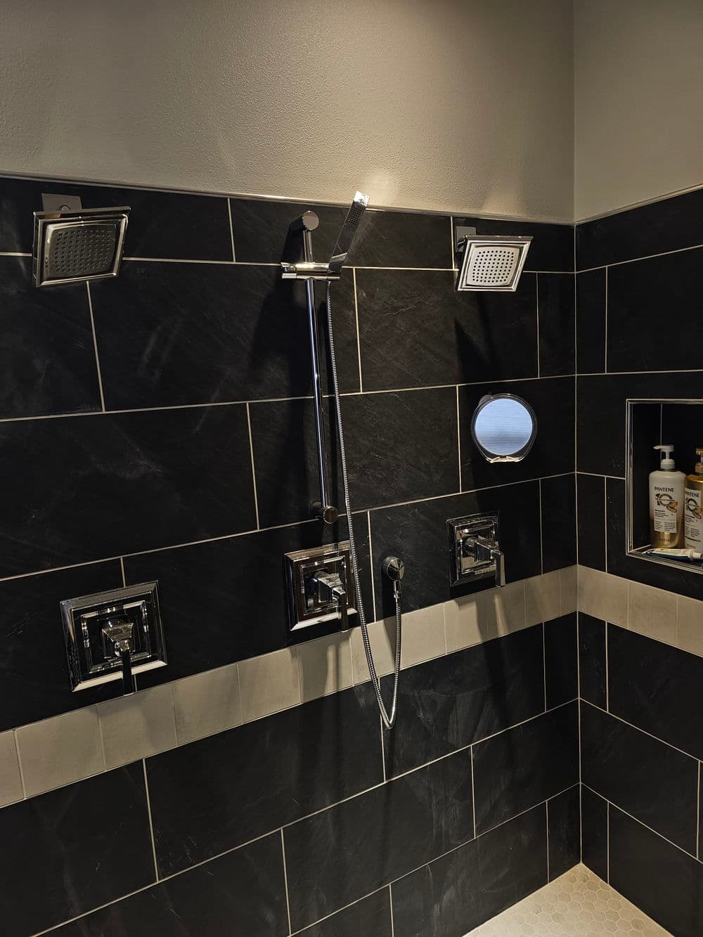 Modern shower design with dual rain shower heads and sleek chrome fixtures on black tiled walls.