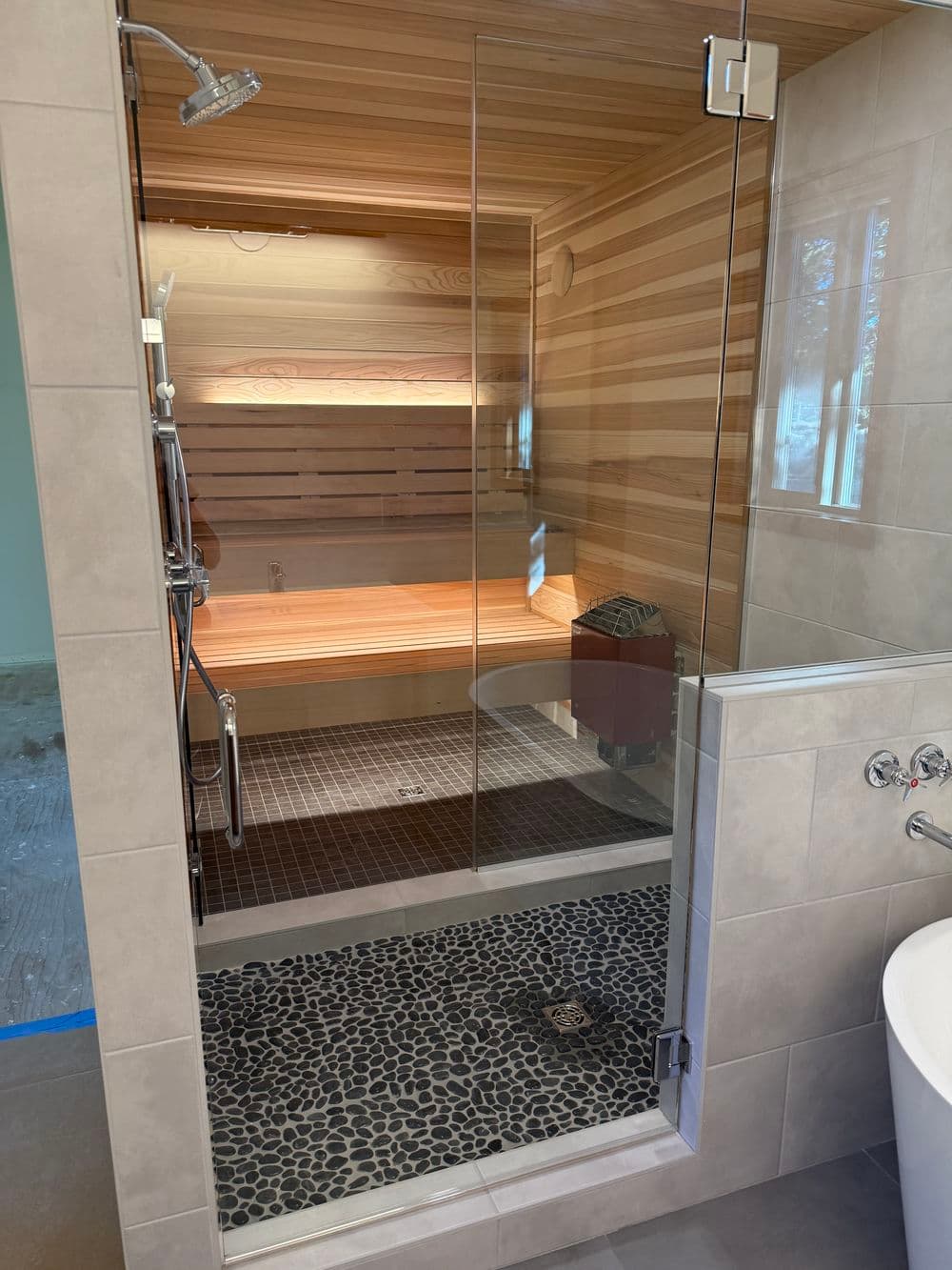 Modern shower with glass enclosure, wooden accents, stone flooring, and stylish fixtures.