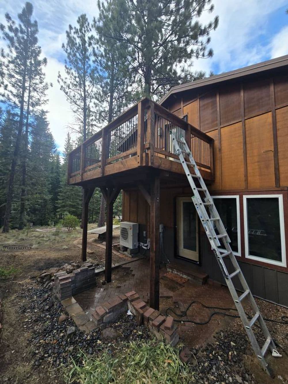 Wooden balcony with ladder at a cabin surrounded by tall pine trees.