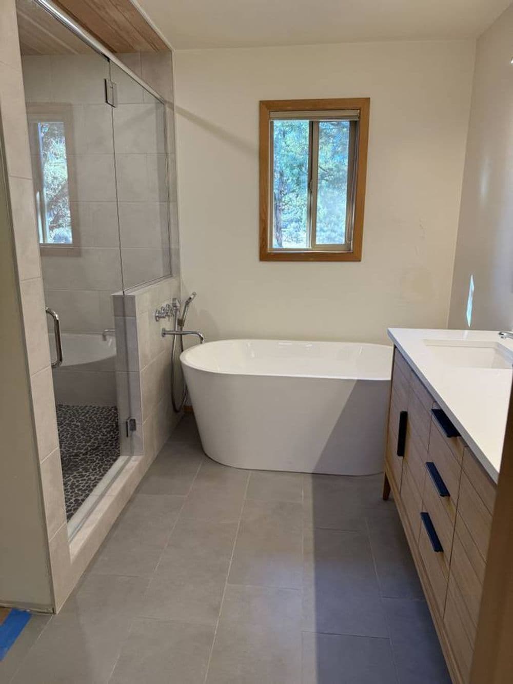 Modern bathroom featuring a freestanding tub, glass shower, and wooden vanity. Natural light from window.
