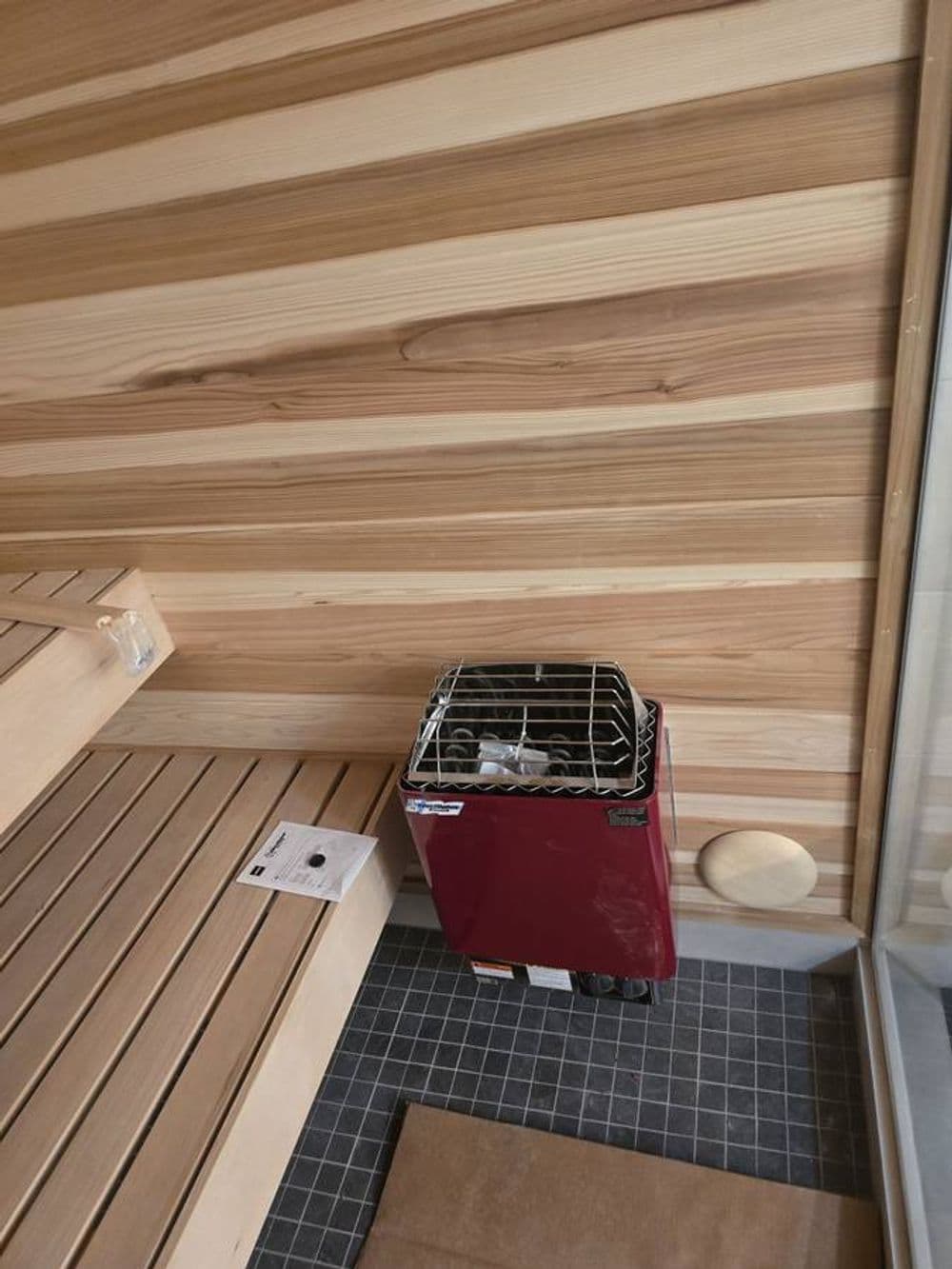 Portable sauna heater on wooden bench in a modern sauna setting. Wood paneling background.