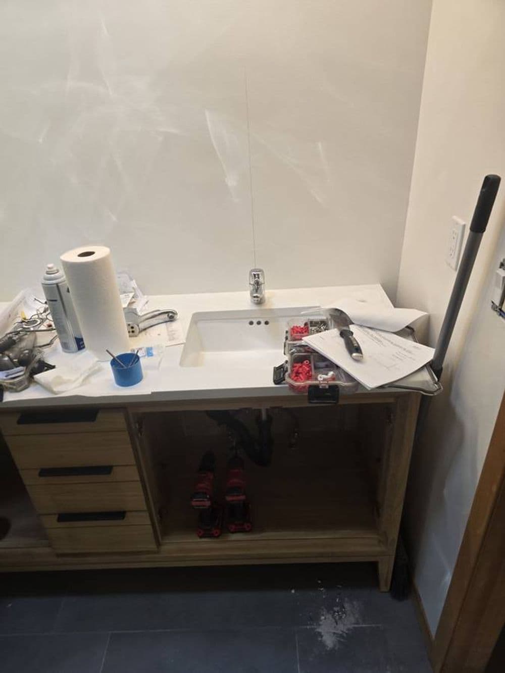 Unfinished kitchen sink area with tools, paperwork, and cleaning supplies on countertop.