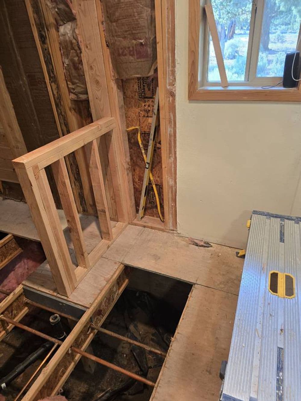Interior home renovation with exposed framing, unfinished floor, and tools visible.