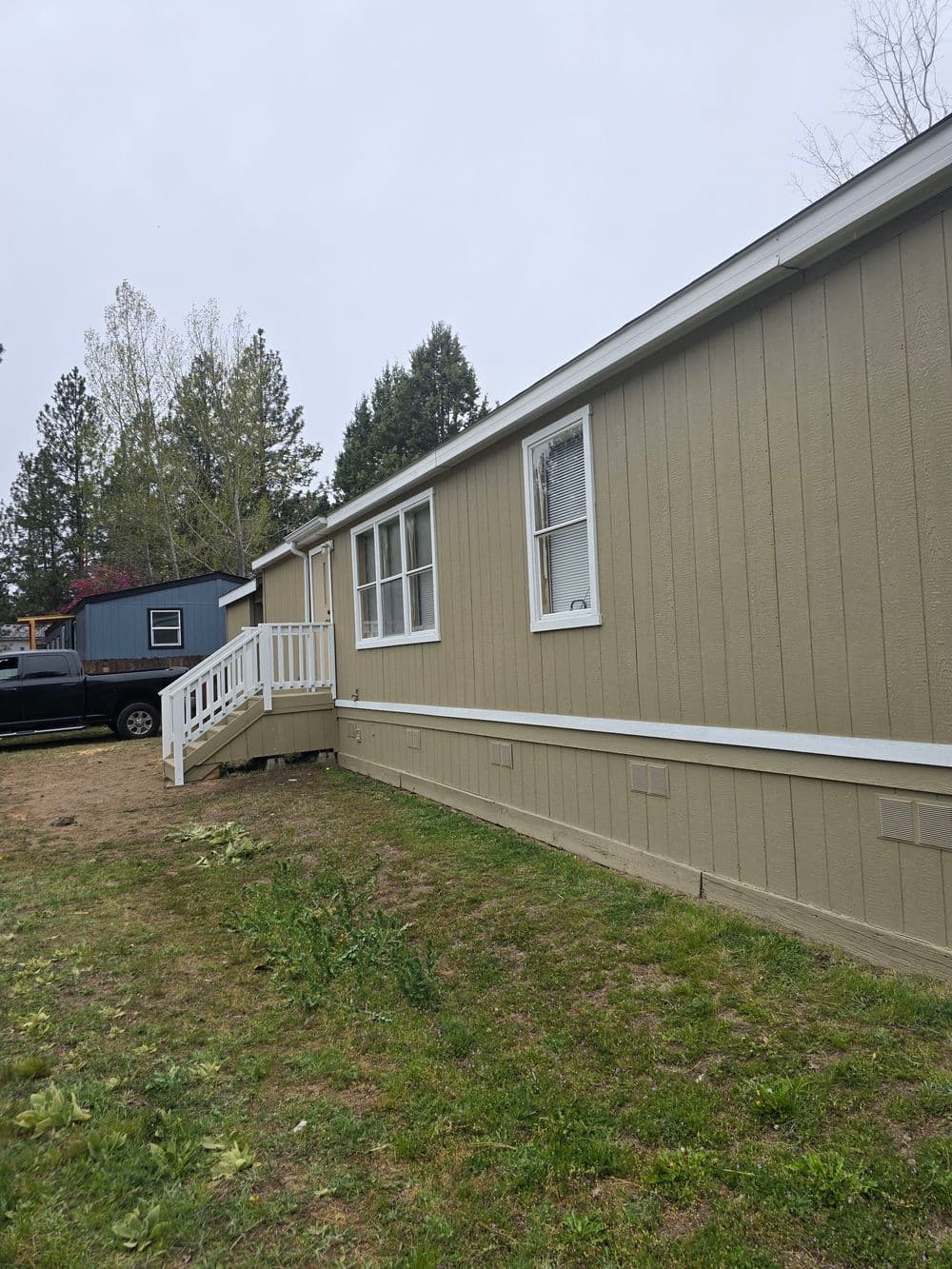 Side view of a beige mobile home with a white porch in a rural setting.