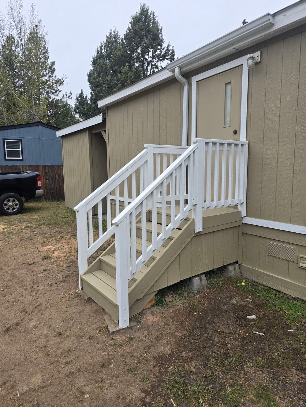 White wooden steps leading to a door of a tan house with a gravel pathway.