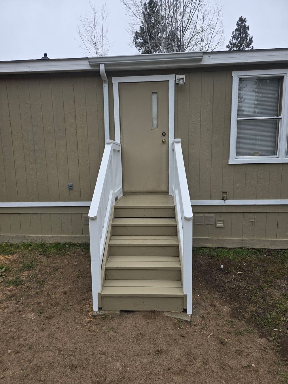 Exterior view of a beige building with a single door and white railings on wooden stairs.