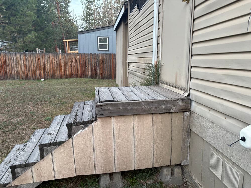 Wooden steps leading to a house, showing wear and a backyard with a fence in the background.