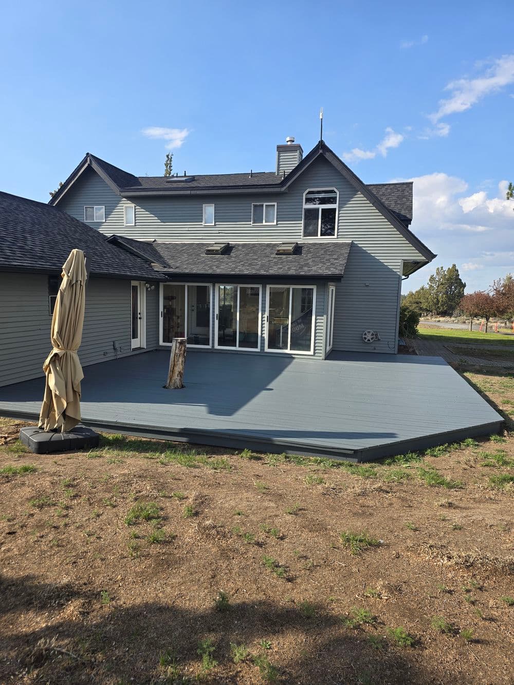 Modern home exterior with large deck area, gray siding, and minimal landscaping.