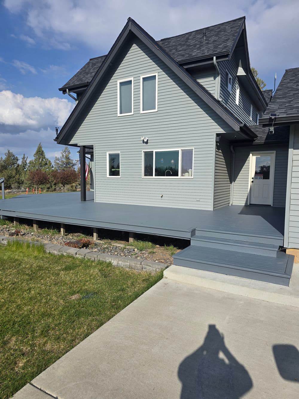 Modern gray house with a spacious wooden deck and lawn under a blue sky.
