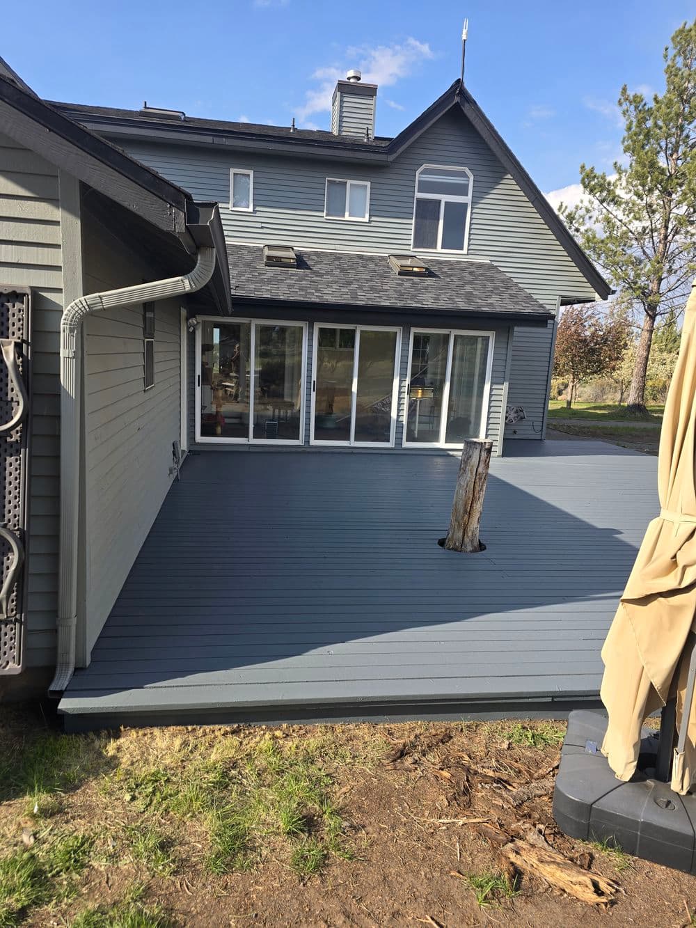 Modern backyard deck with gray composite flooring, adjacent house, and views of green trees.