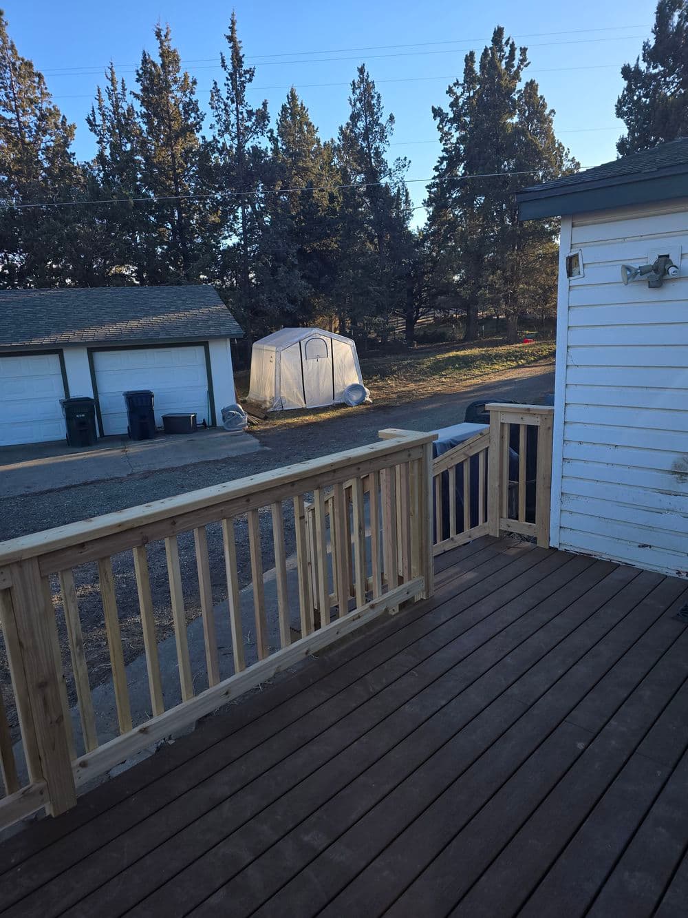 View from a deck showing trees, a tent, and nearby garages in a sunny outdoor setting.