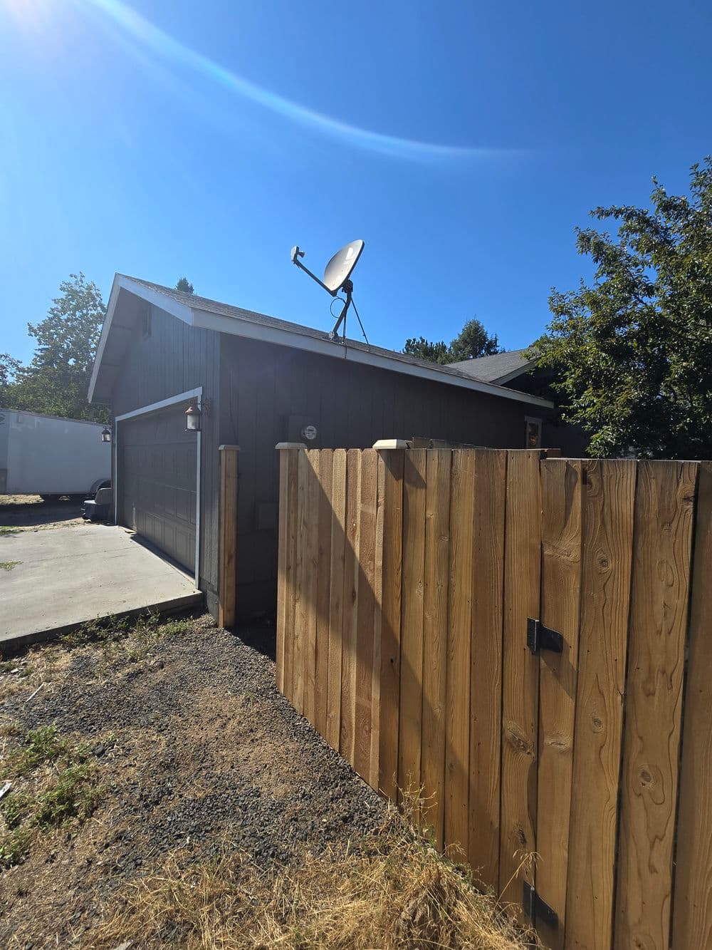 Side view of a home with a wooden fence and satellite dish under a clear blue sky.