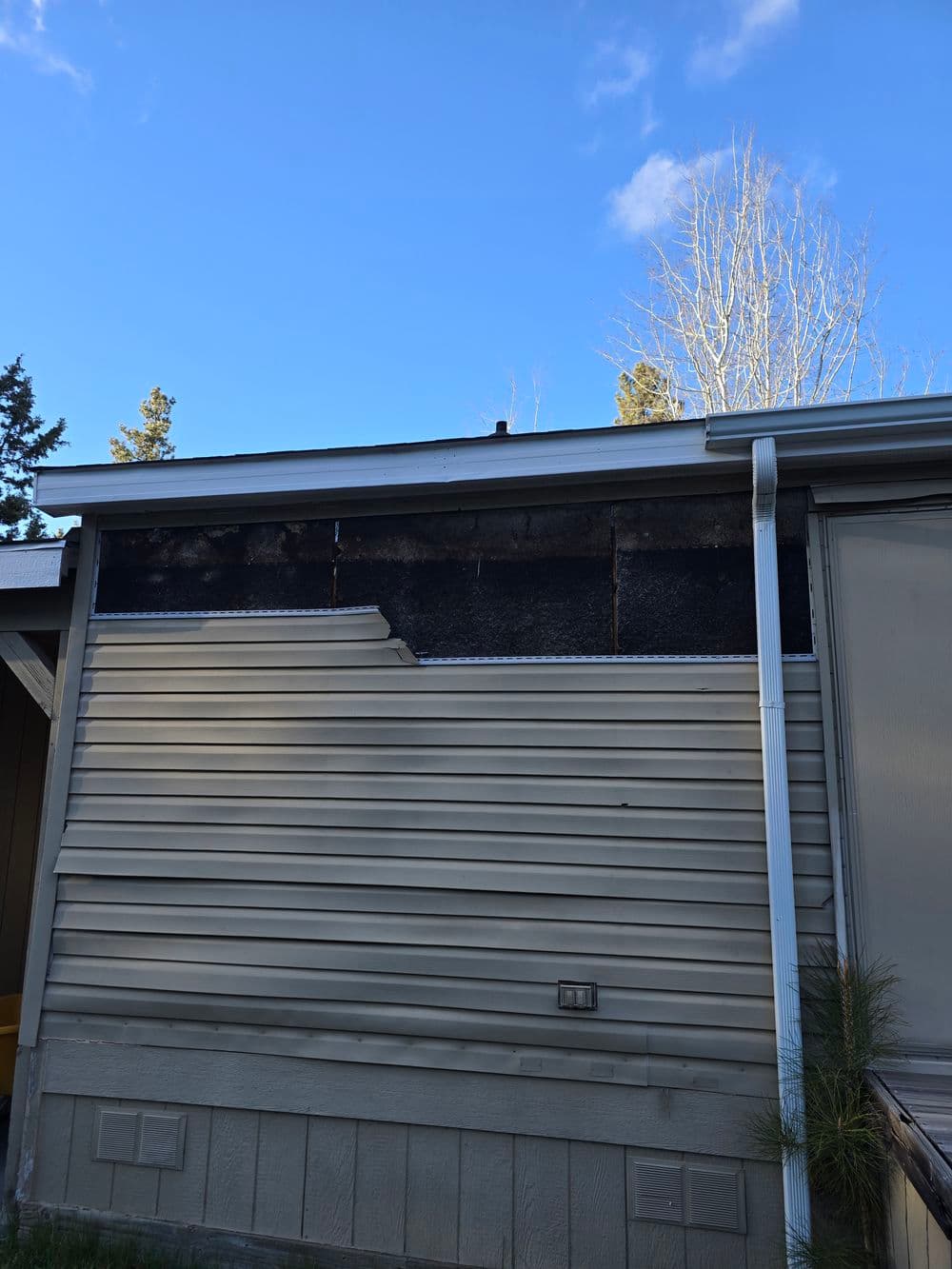 Damaged exterior siding of a house with fire-related char marks and a clear blue sky.