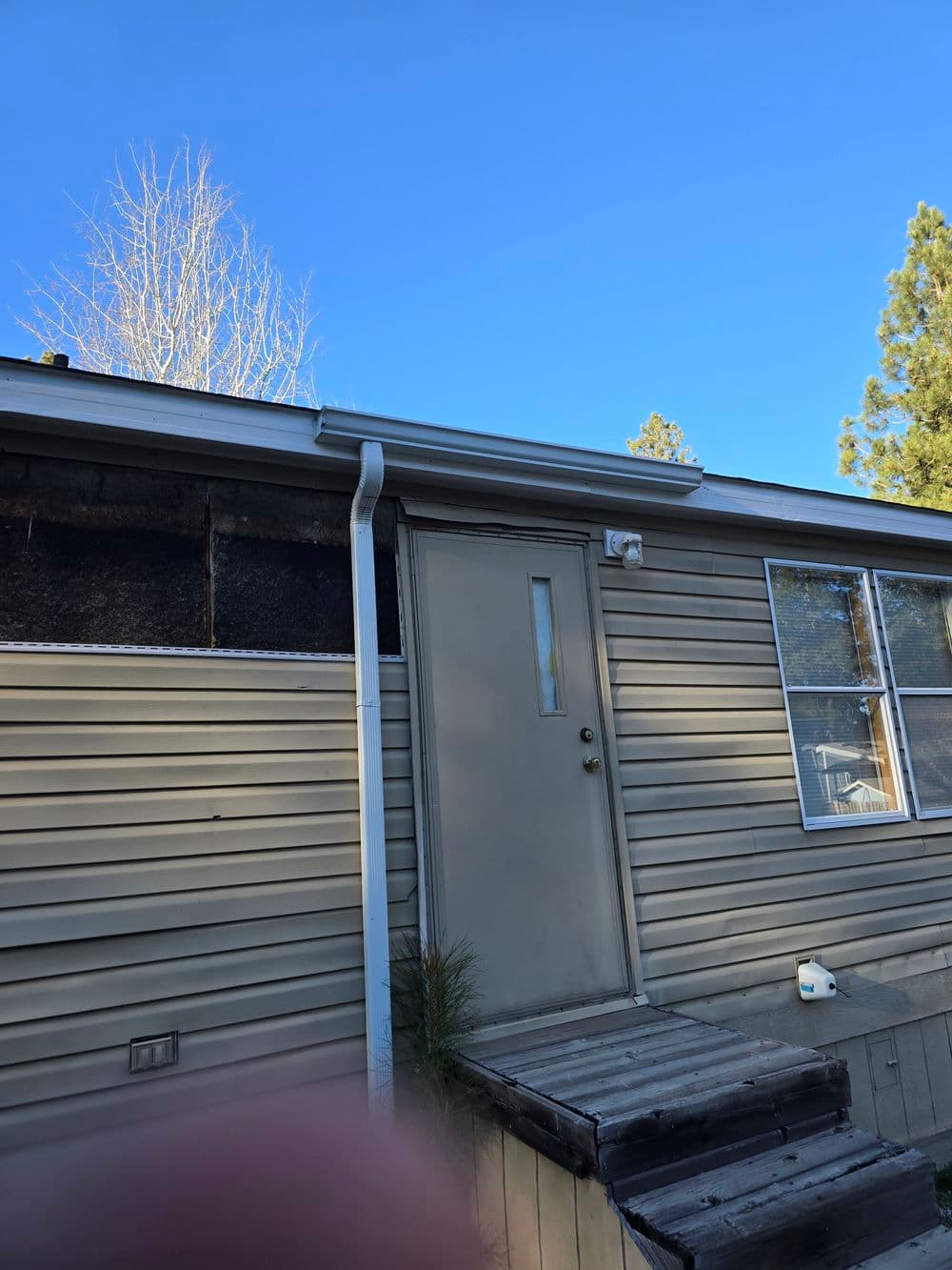 Exterior of a mobile home with a gray door and wooden steps under a clear blue sky.