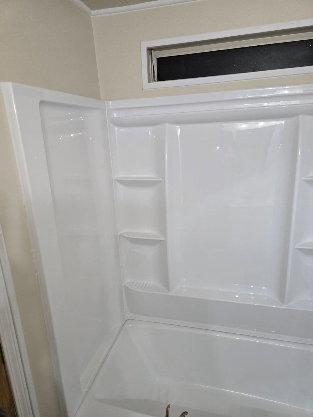 Modern white shower unit with built-in shelves and sliding glass door in clean bathroom setting.