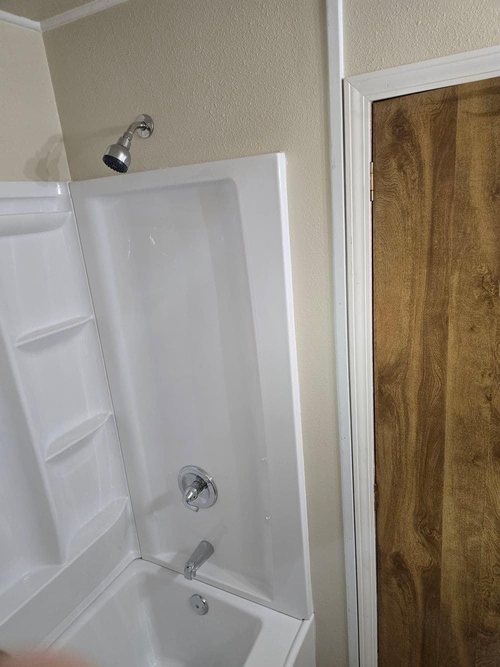Modern white bathtub with showerhead, featuring light walls and a wooden door.