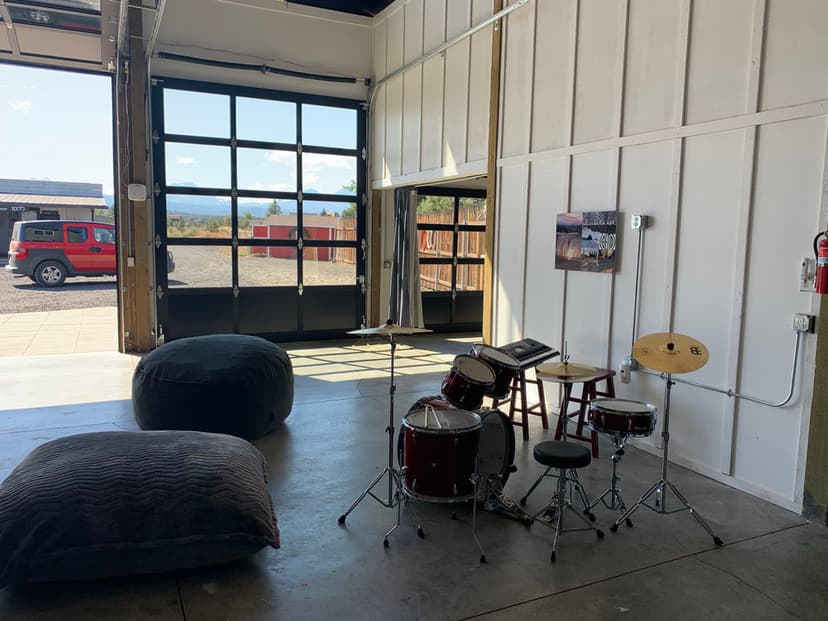 Drum set in a spacious garage with open door, bean bags, and scenic outdoor view.