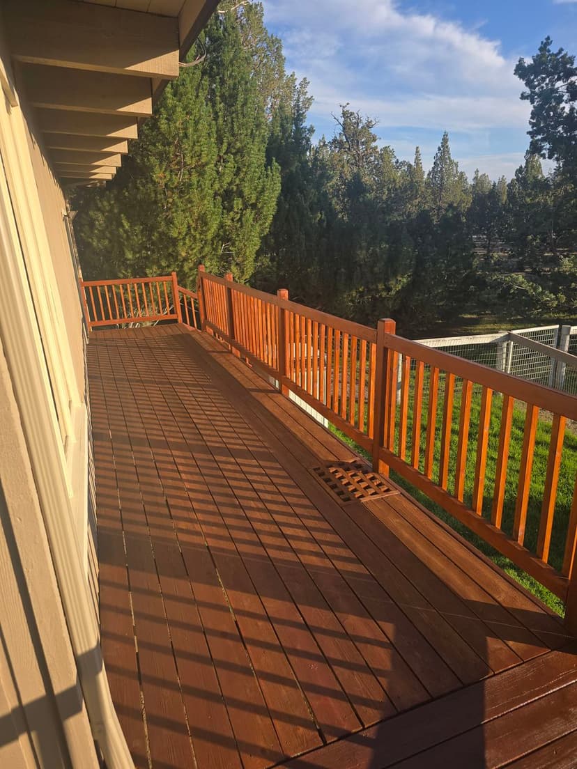 Spacious wooden deck with orange railings surrounded by lush greenery and blue sky.
