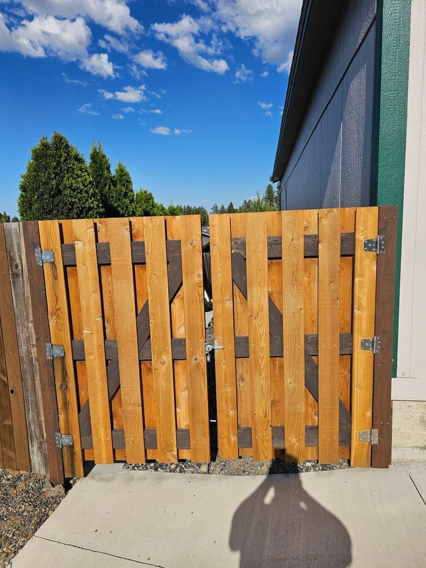 Wooden garden gate with horizontal slats under a clear blue sky, adjacent to a house.