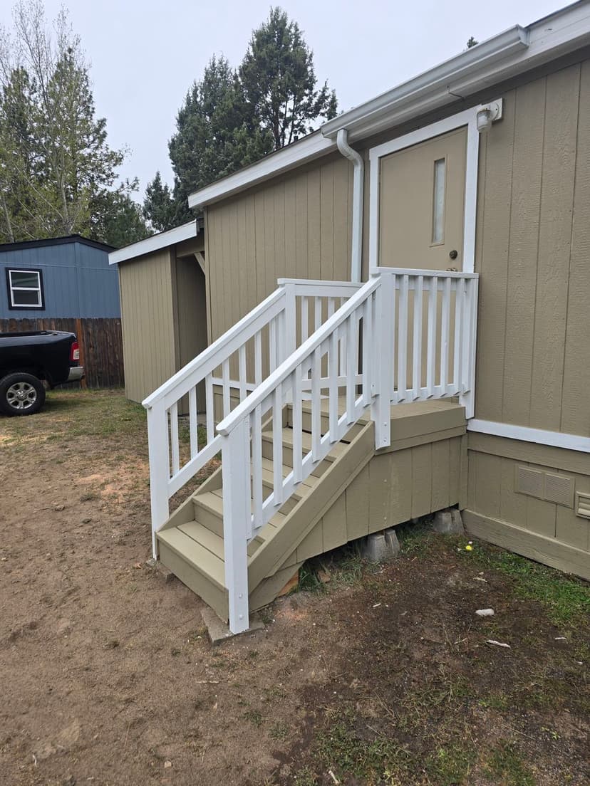 White wooden stairs leading to a home's door, surrounded by a dirt pathway and greenery.