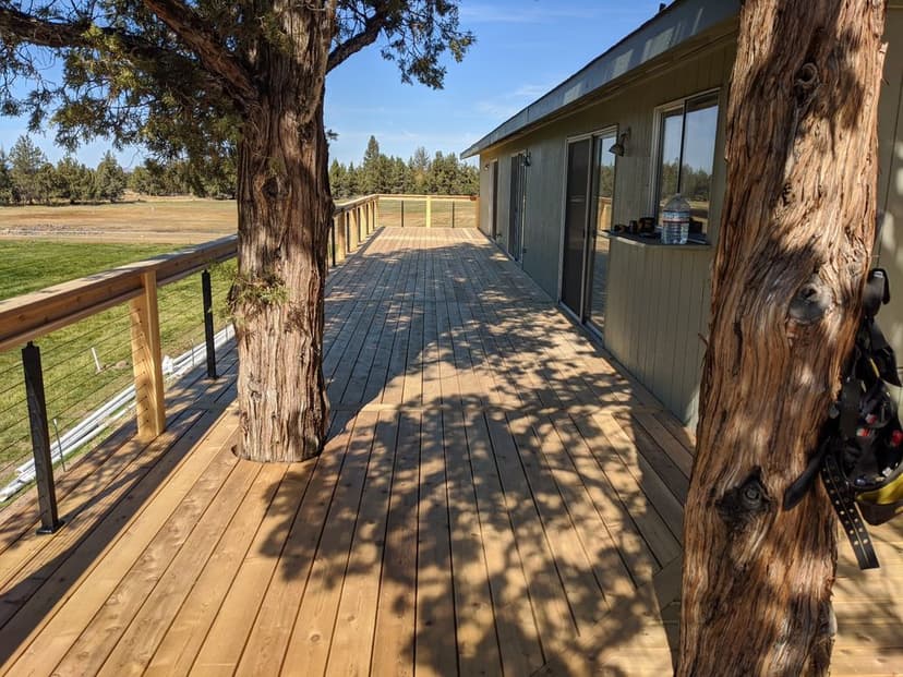 Spacious wooden deck beside a house, framed by trees and overlooking a green landscape.