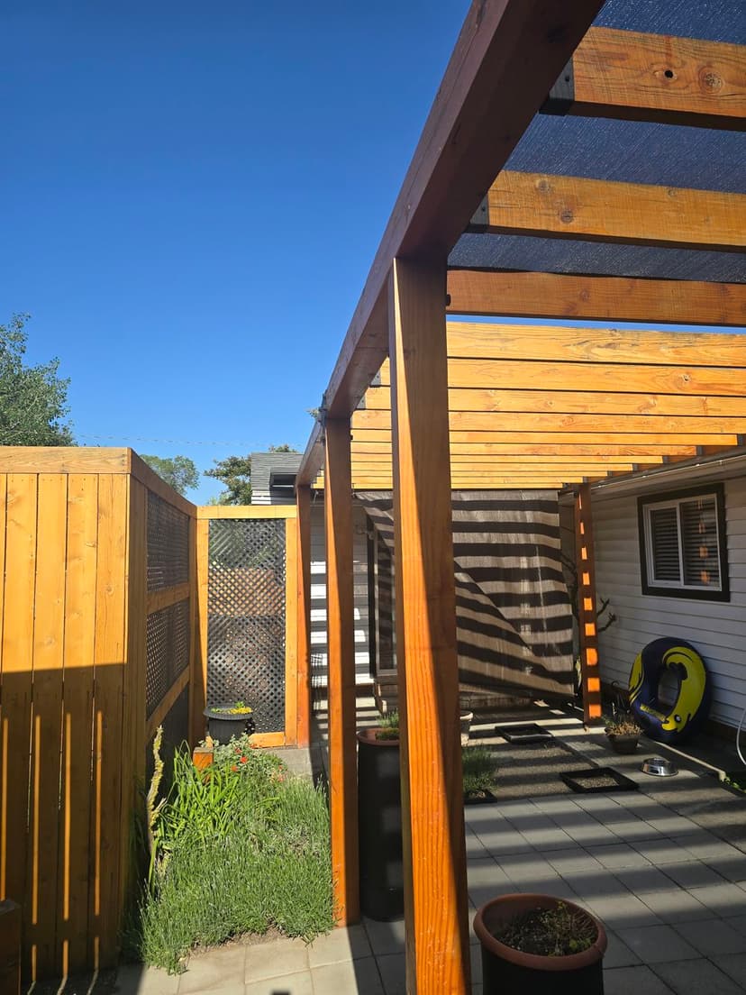 Modern patio design featuring wooden beams, fencing, and a clear blue sky.